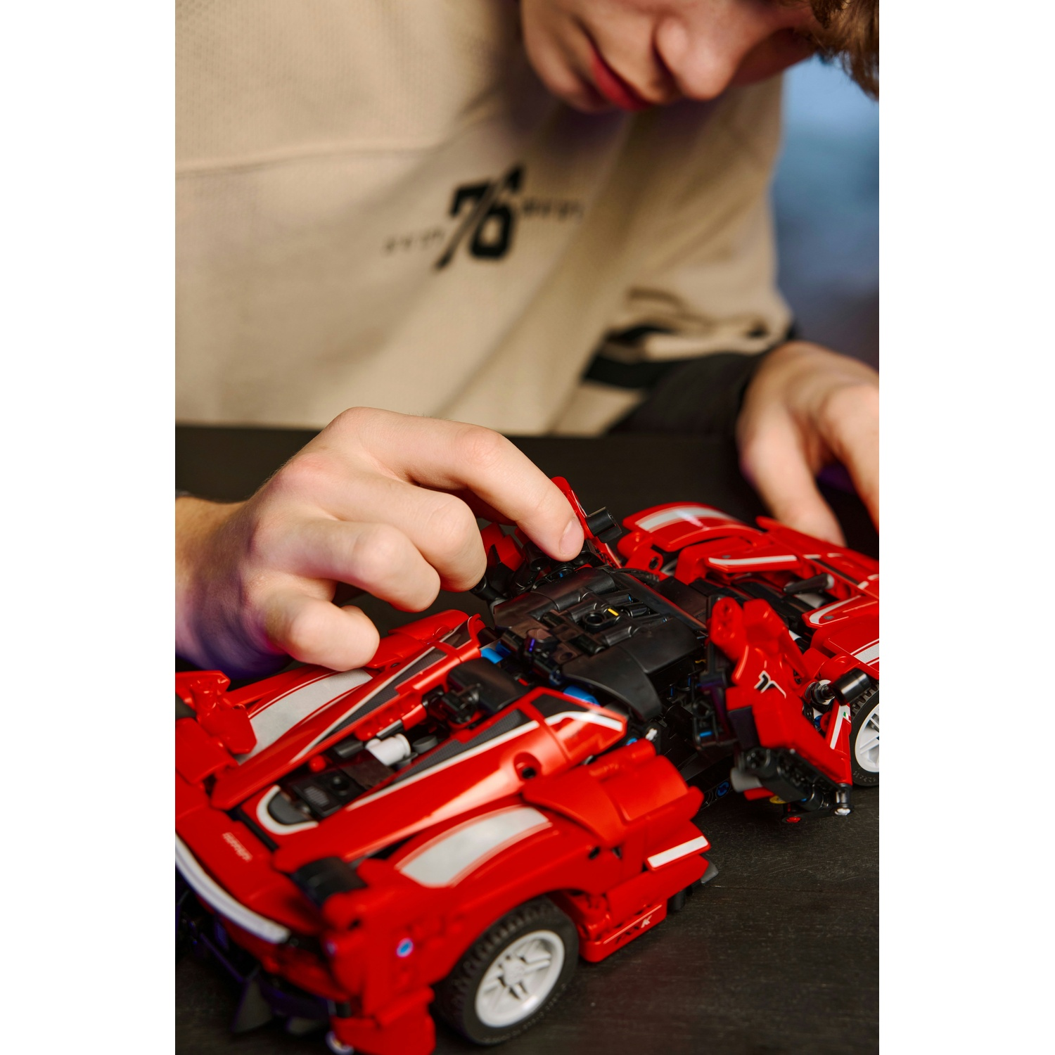 Una persona sta assemblando un'auto giocattolo rossa. L'auto è su una superficie nera. La persona indossa un maglione beige.