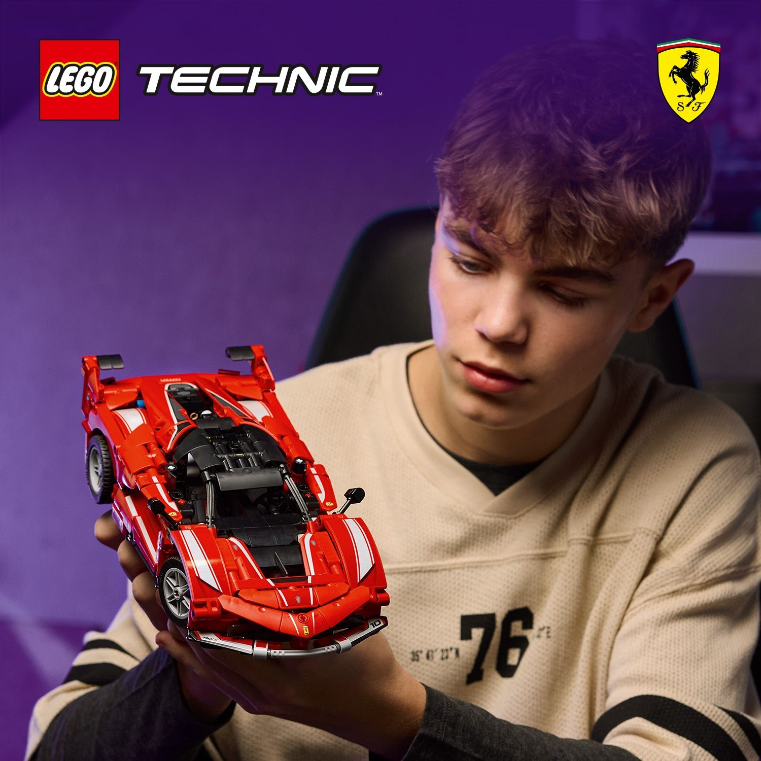 Un giovane tiene in mano una Ferrari Lego Technic rossa. La persona indossa una maglia beige con il numero 76. Lo sfondo è viola.