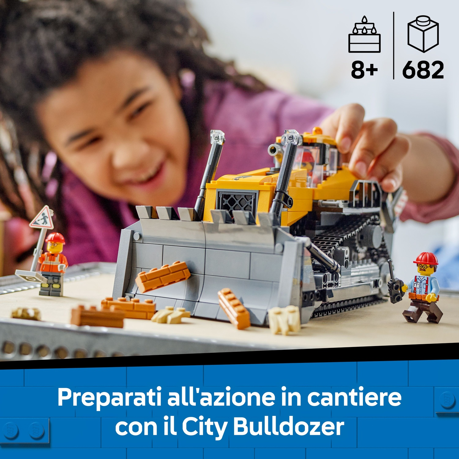 Un bambino gioca con un modello Lego di bulldozer giallo e grigio. Ci sono personaggi e mattoncini Lego di operai edili. Il set è per bambini dagli 8 anni in su.
