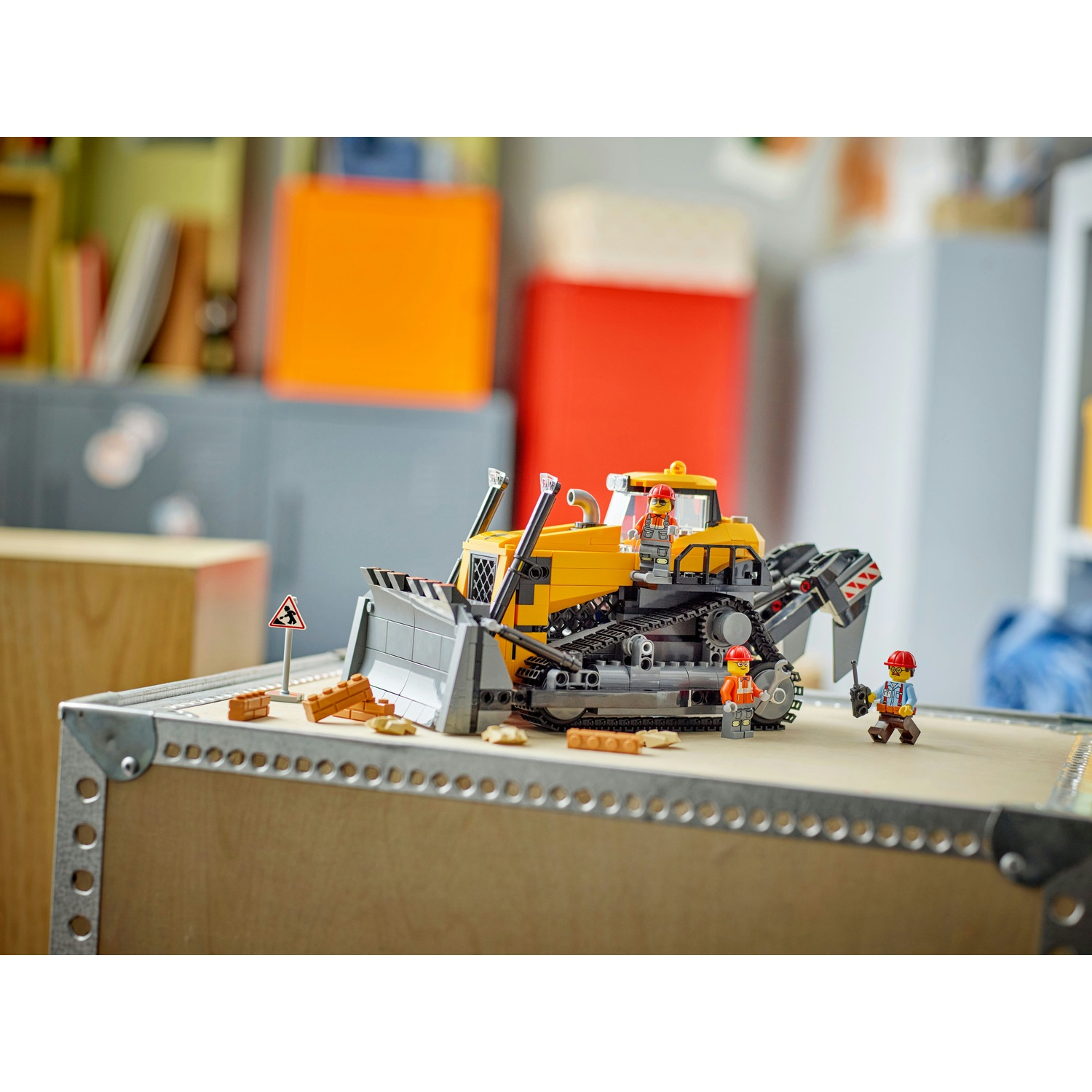Una scena di costruzione Lego con un bulldozer giallo, tre minifigure e segnali di costruzione su una superficie di legno.