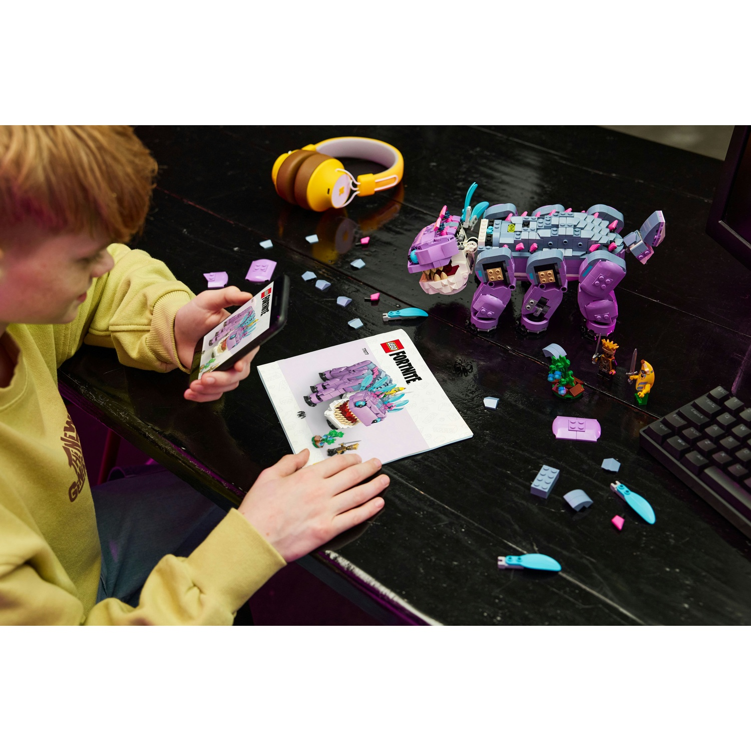 Una persona sta costruendo un set Lego, con le istruzioni aperte e un telefono che mostra le istruzioni. Un set Lego è assemblato sul tavolo.