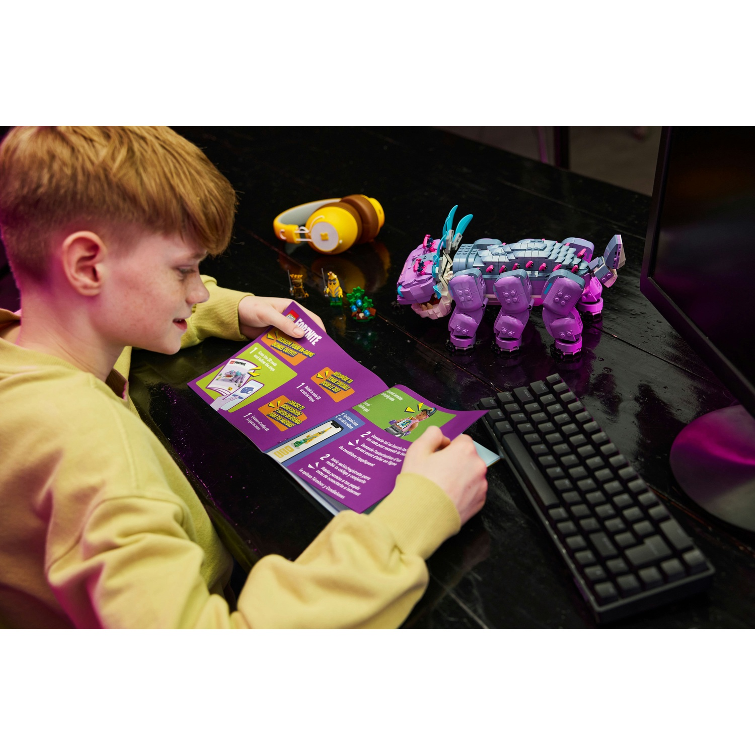 Un ragazzo guarda una guida del gioco Fortnite. Una creatura giocattolo, una tastiera e un'arma giocattolo sono sul tavolo.