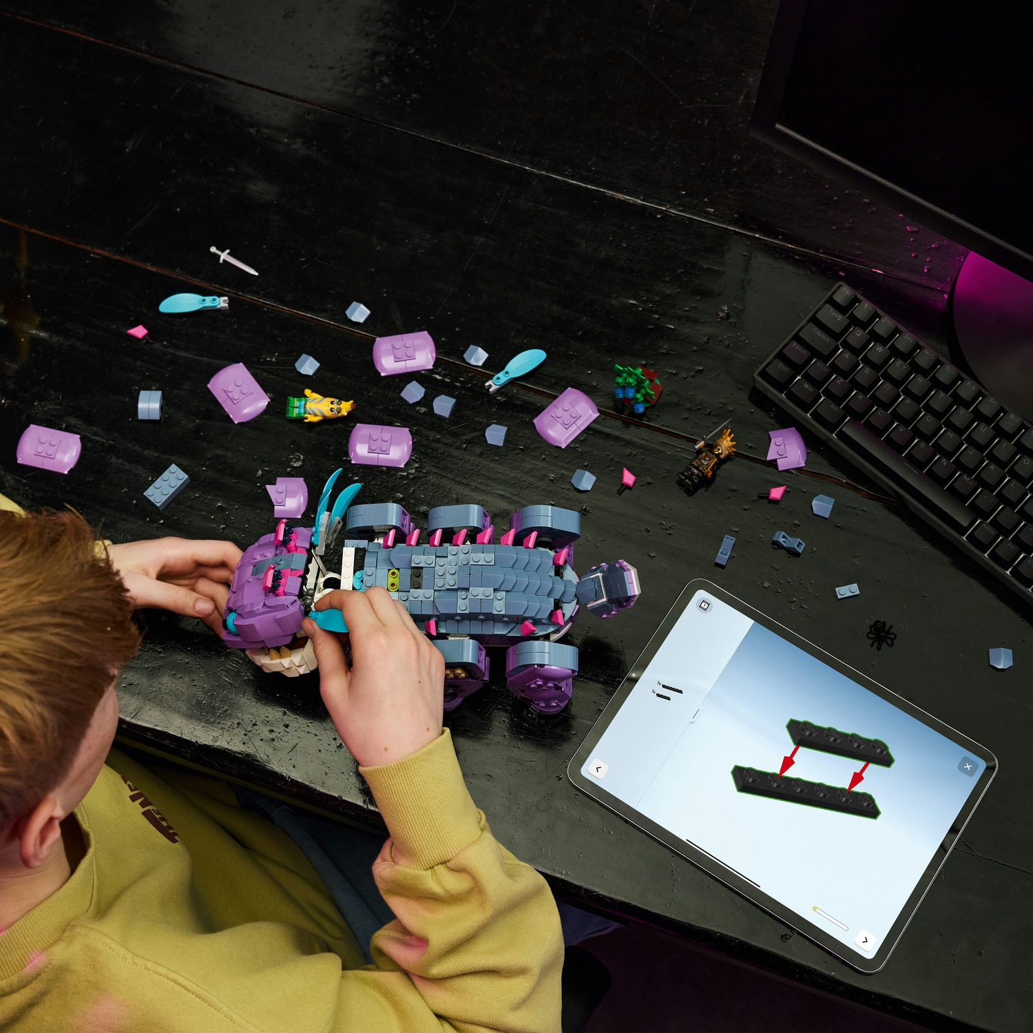 Una persona assembla un set Lego su un tavolo nero con un tablet che mostra le istruzioni, una tastiera e pezzi Lego sparsi.