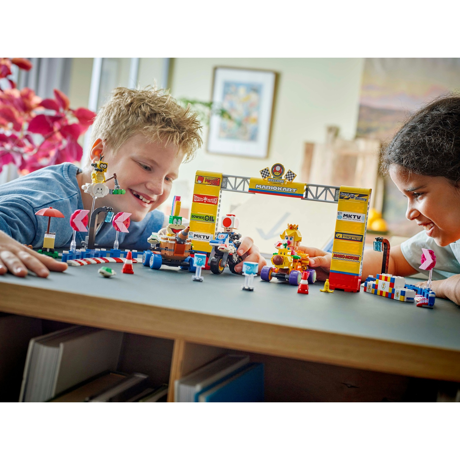 Due bambini giocano con un set Lego Mario Kart. Il set presenta un circuito, auto e personaggi come Peach e Toad.