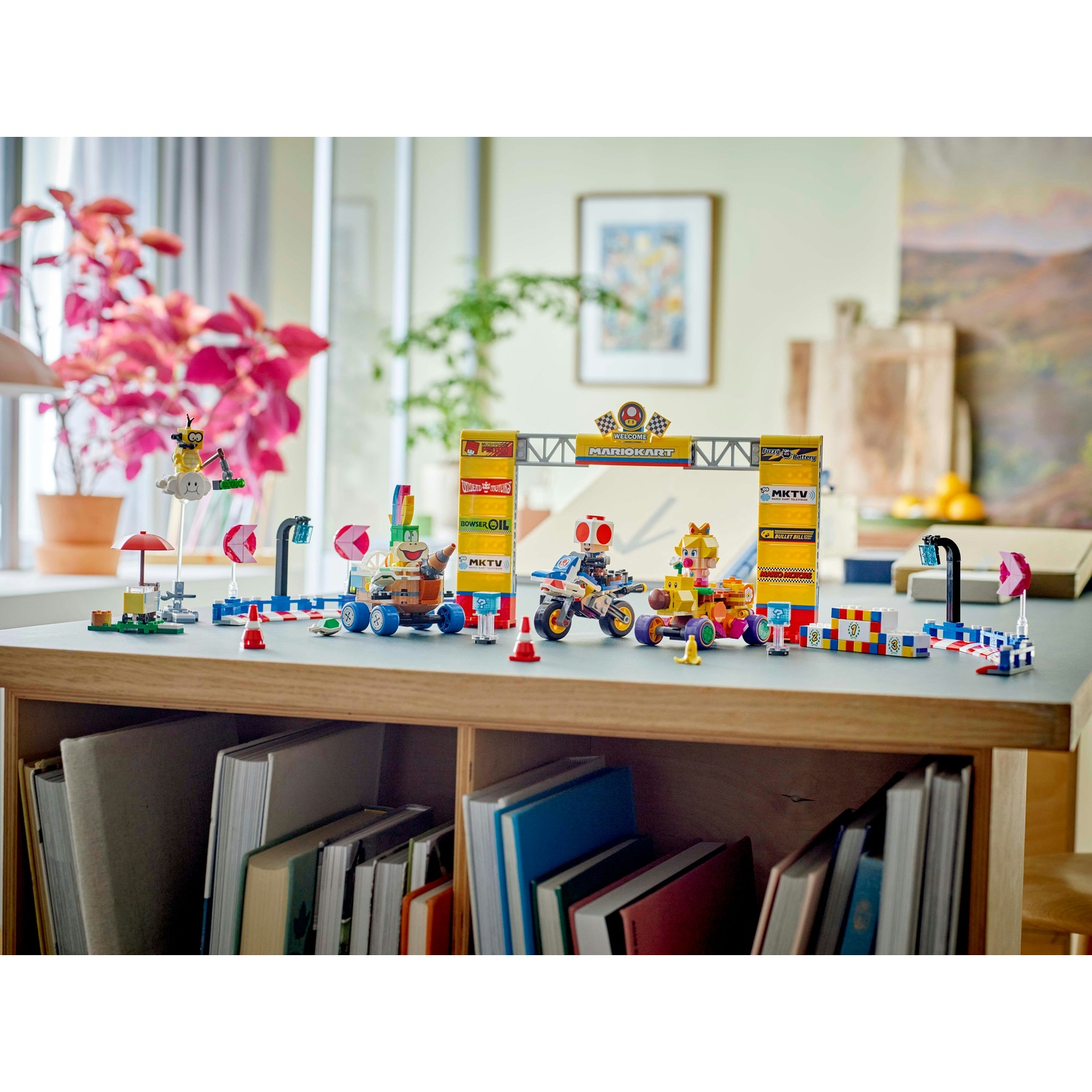 Un colorato set LEGO Mario Kart su un tavolo, con minifigure ed elementi della pista. Sotto il tavolo ci sono delle librerie.