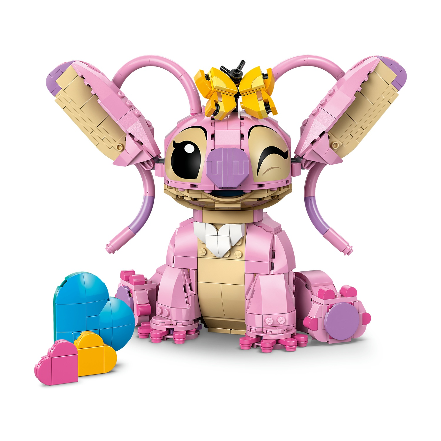 Un personaggio Lego di Angel, con colori rosa e beige, che ammicca. Ci sono forme di cuore blu, gialle e rosa in primo piano.