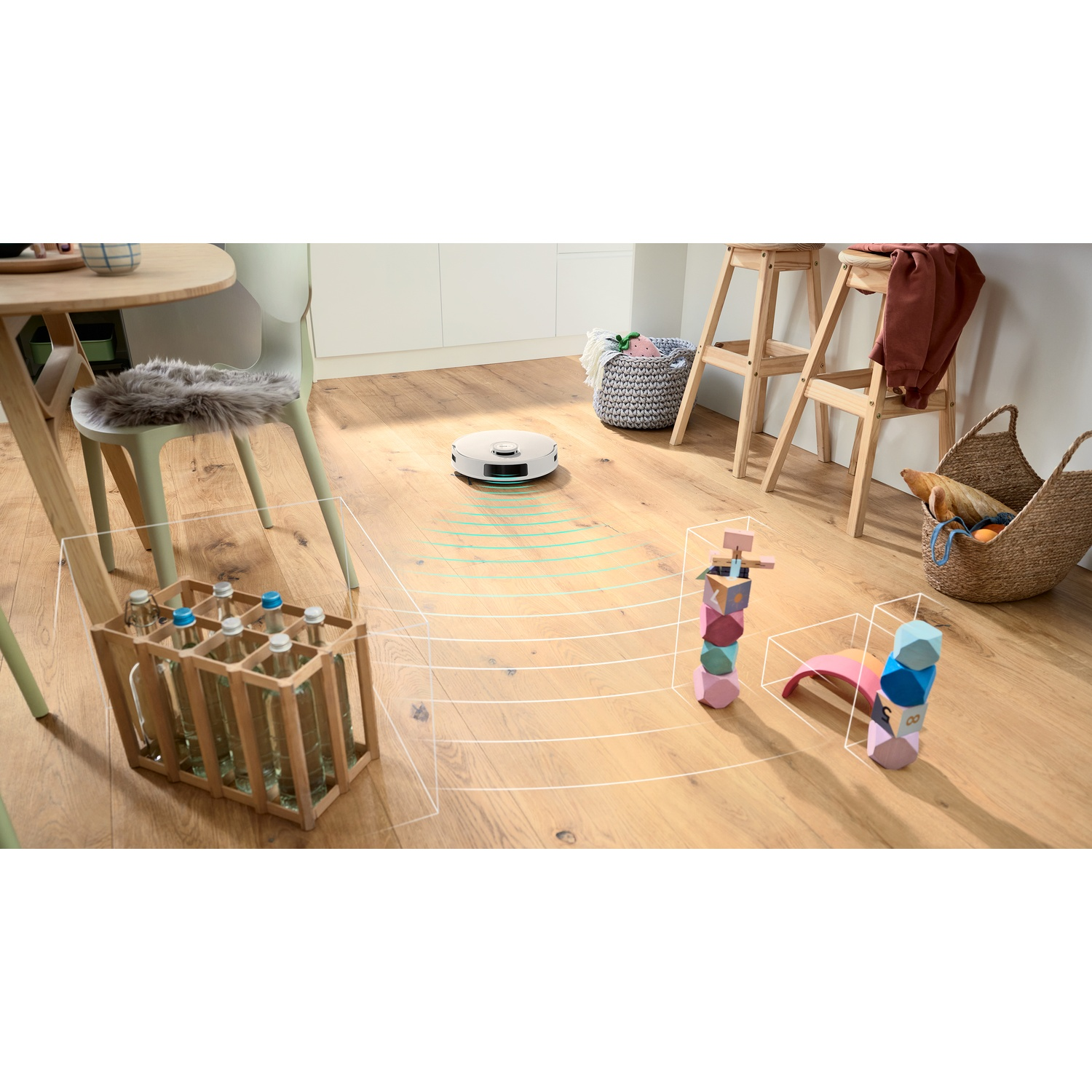 Een robotstofzuiger maakt een houten vloer schoon. Er is een houten krat met flessen, speelgoed, stoelen en een mand met items.
