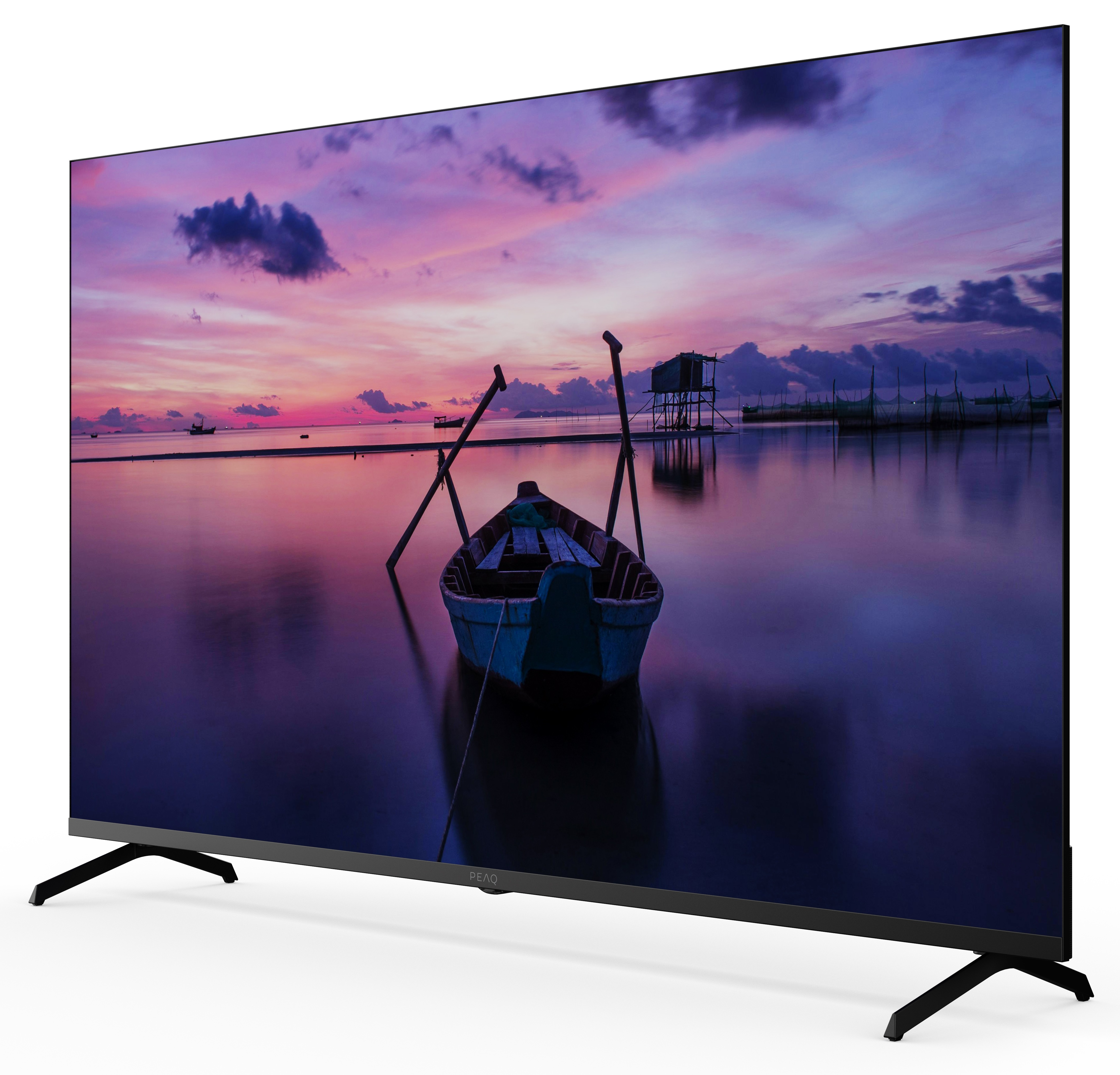 Telewizor wyświetla scenę zachodu słońca z łodzią w wodzie. Telewizor jest czarny z czarnymi nogami na białym tle.