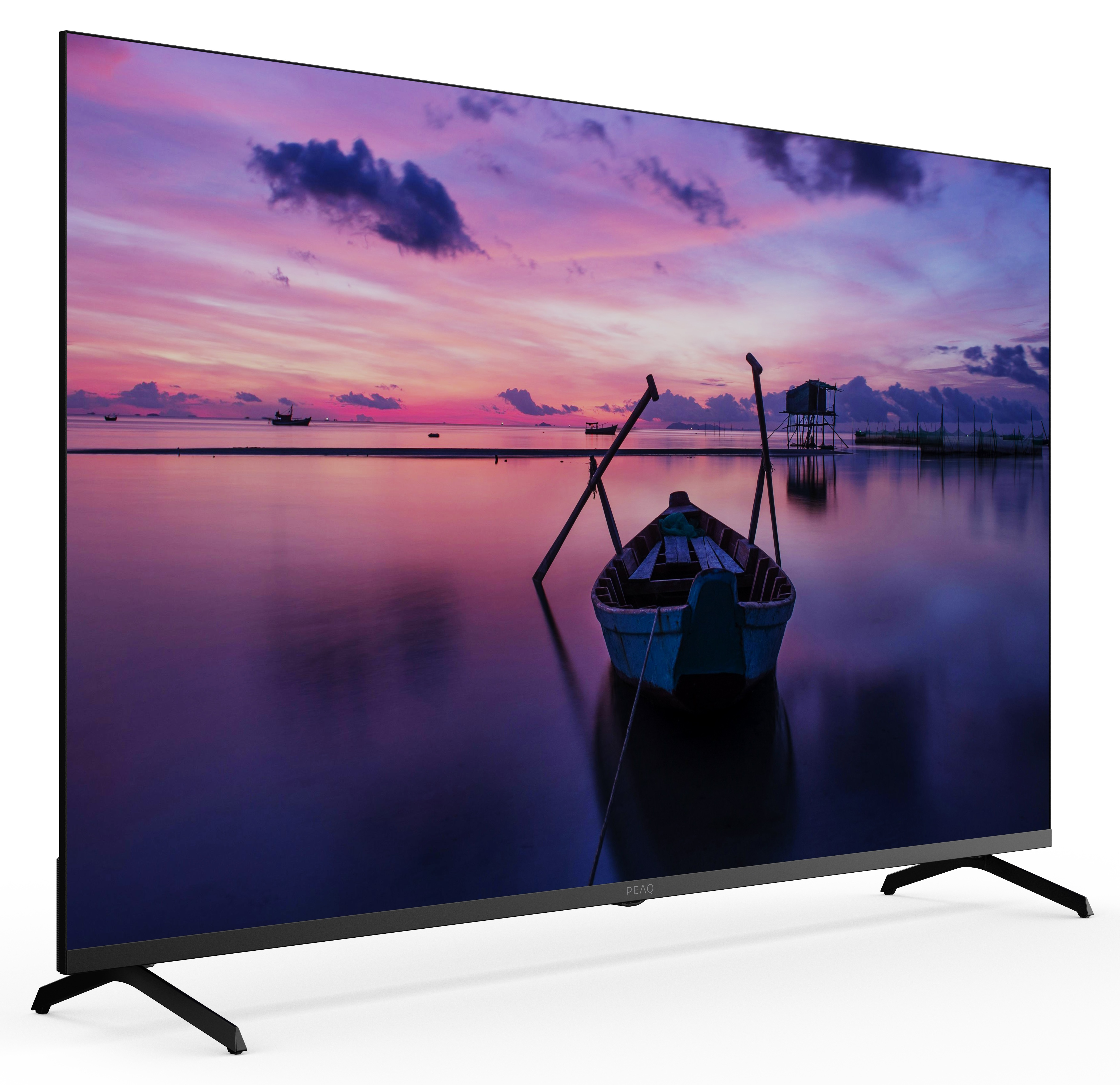 Telewizor wyświetla scenę zachodu słońca z łodzią w wodzie. Telewizor jest ustawiony pod kątem na białej powierzchni.