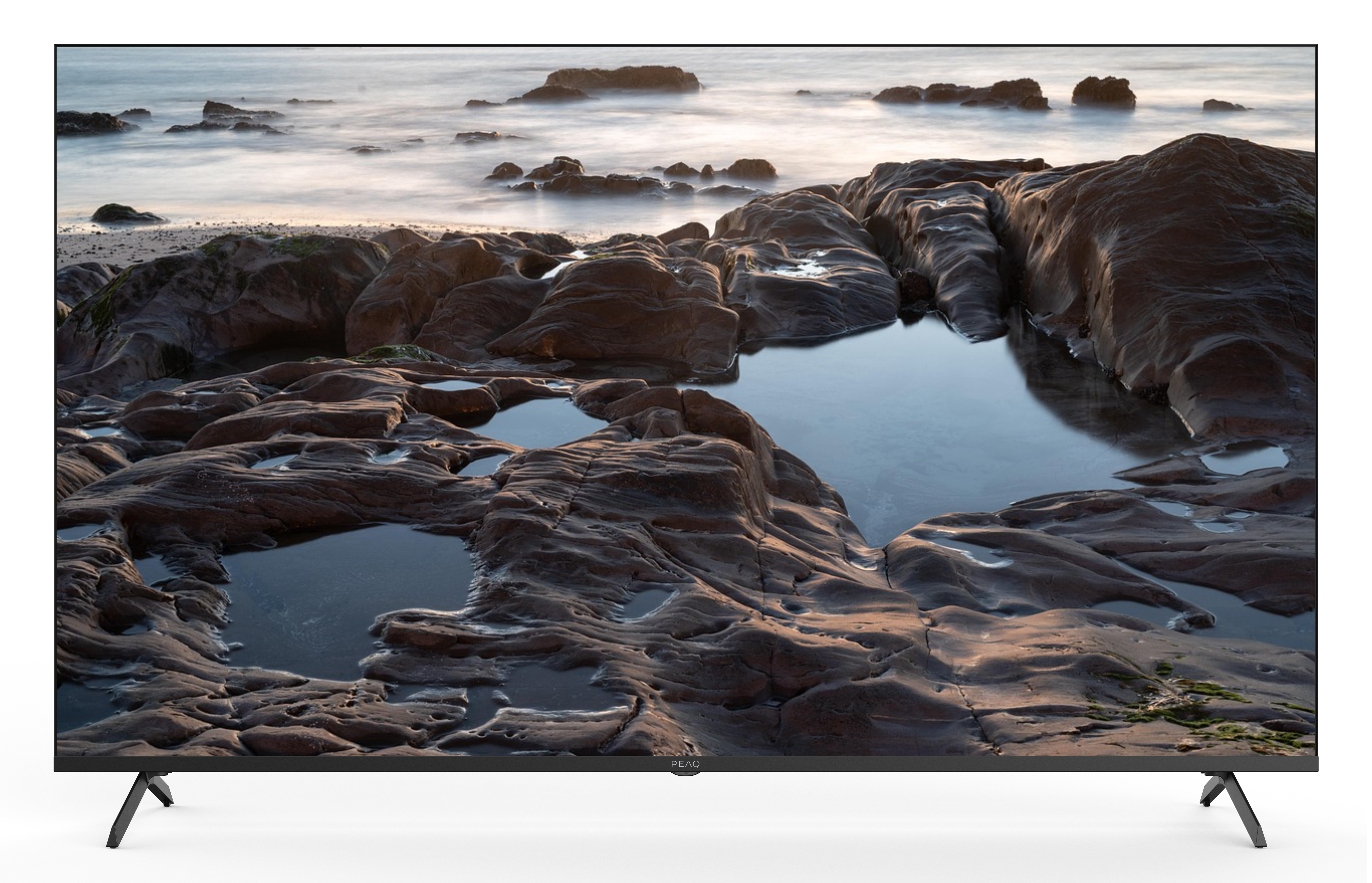 Telewizor przedstawia skaliste wybrzeże z basenami pływowymi i rozmytą wodą w tle. Skały są brązowe.