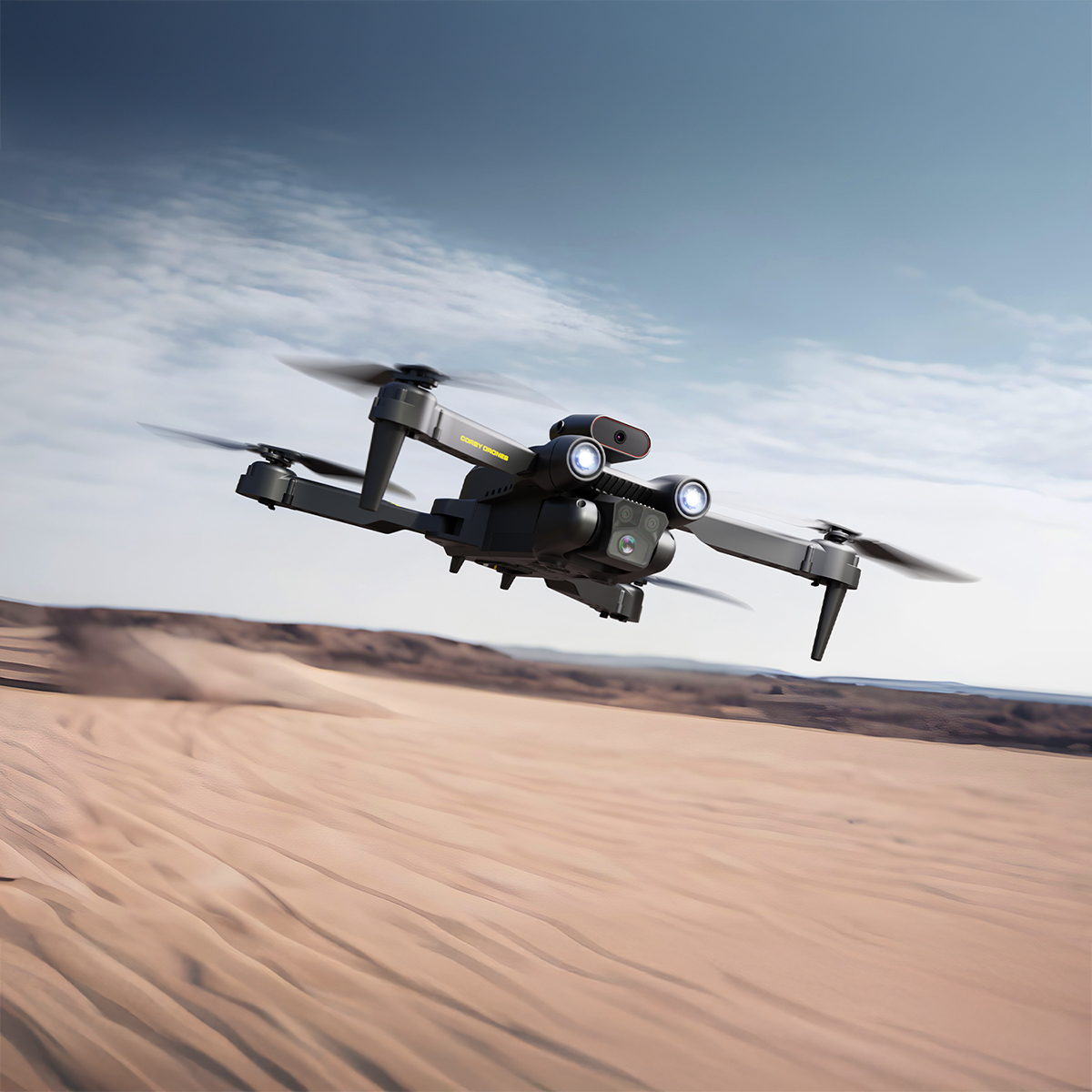 Siyah bir drone çöl manzarası üzerinde uçuyor. Dronun dört pervanesi ve bir kamerası var. Gökyüzü bulutlarla mavi.