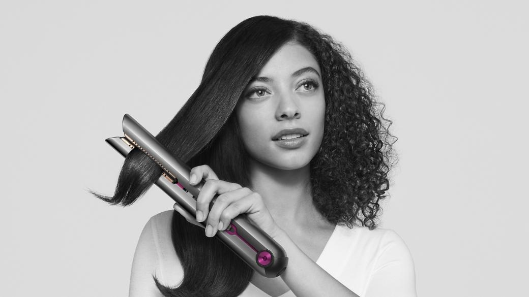 Kobieta używa prostownicy do włosów. Jedna strona jest prosta, druga kręcona. Patrzy w górę.
