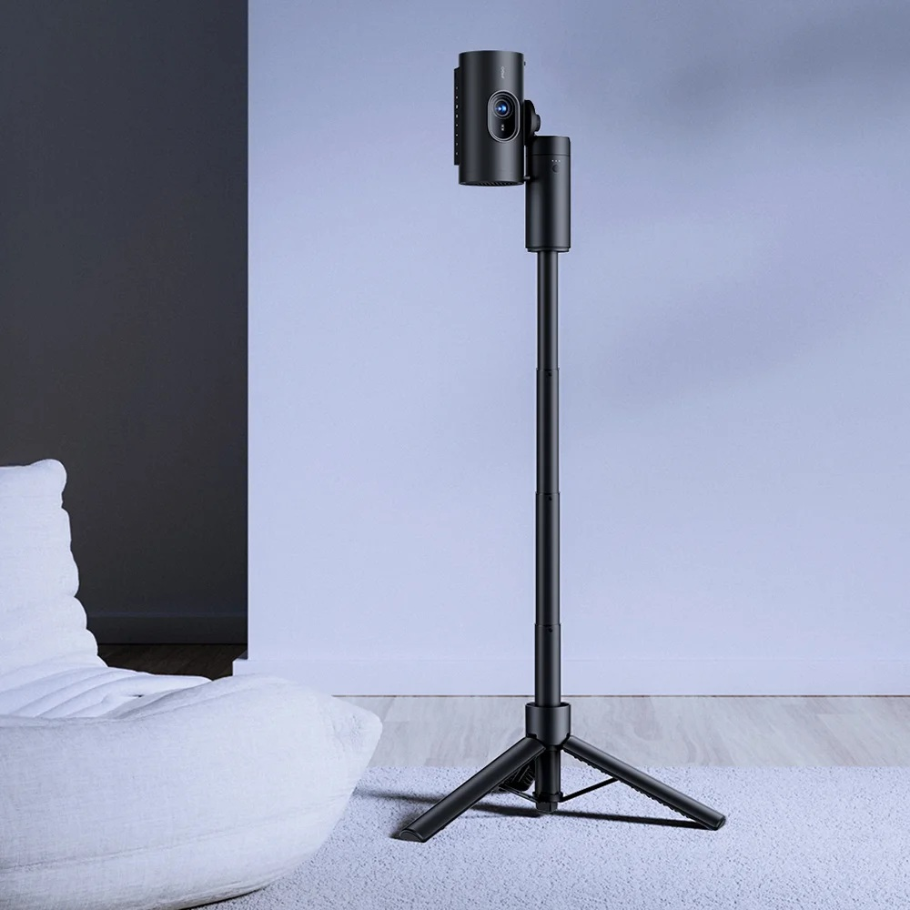 Czarny projektor na statywie. Biała pufa w tle. Ściana jest niebiesko-szara.