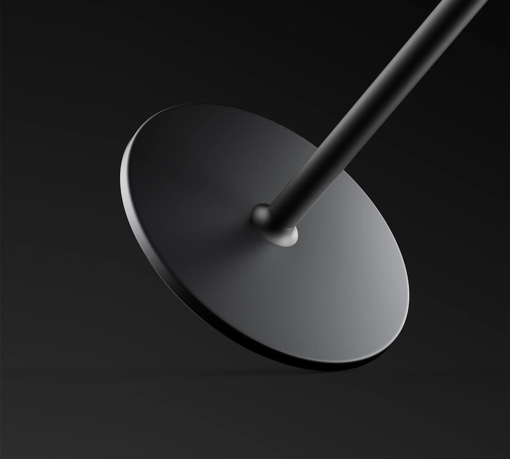 Czarny, okrągły obiekt z trzonem, ustawiony pod kątem na ciemnym tle. Trzon łączy koło.