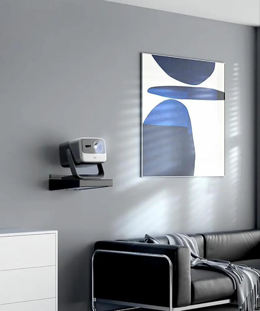 Projektor na uchwycie ściennym, sztuka abstrakcyjna, czarna kanapa, biała komoda i światło słoneczne przez żaluzje.