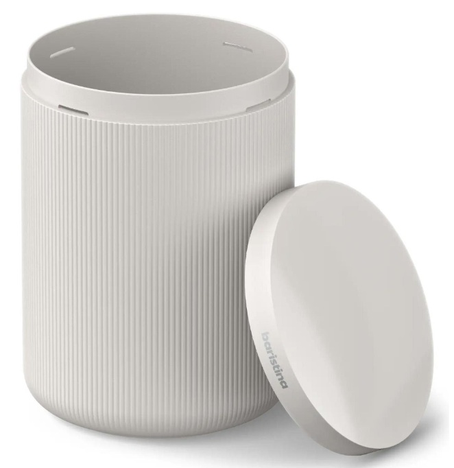 Kremowy, cylindryczny pojemnik z żebrowaną fakturą. Pokrywka zdjęta i lekko z boku, z nadrukiem 'baristina'.