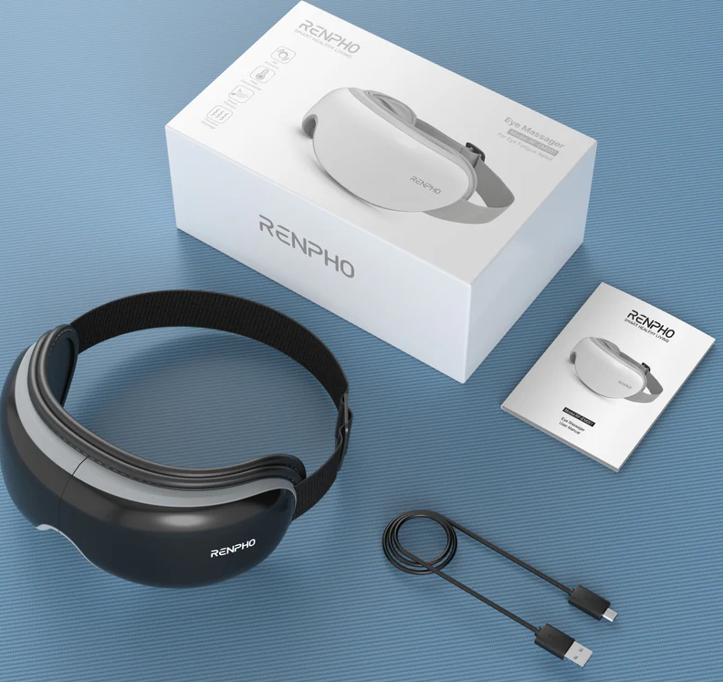 Masażer do oczu i jego pudełko, instrukcja obsługi i kabel ładujący leżą na niebieskiej powierzchni. Masażer jest czarno-biały.