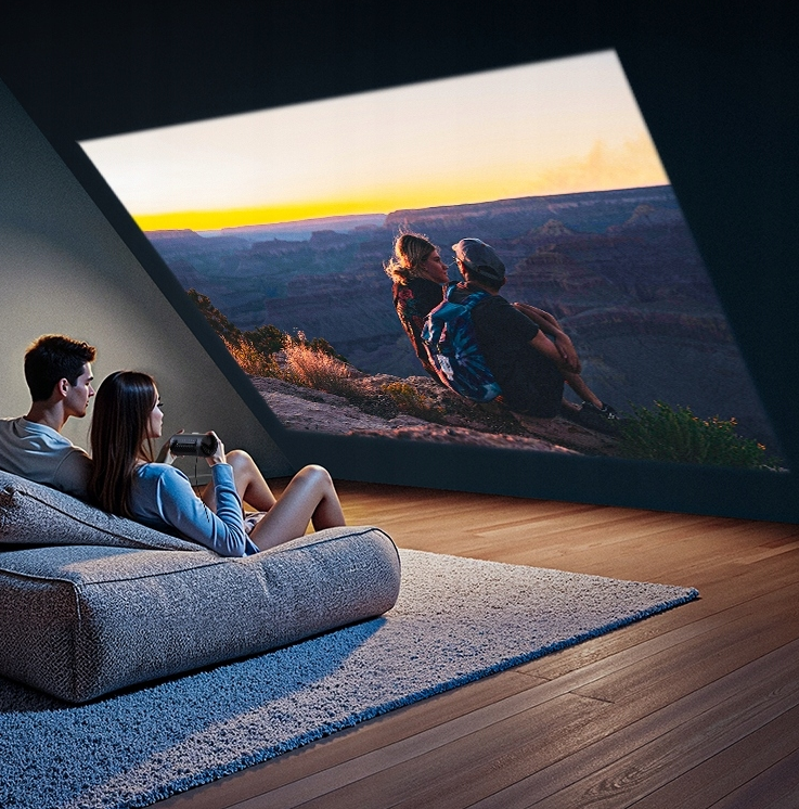 Para ogląda zachód słońca na ekranie, z drugą parą na kanapie na pierwszym planie. Pokój z dywanem i drewnianą podłogą.