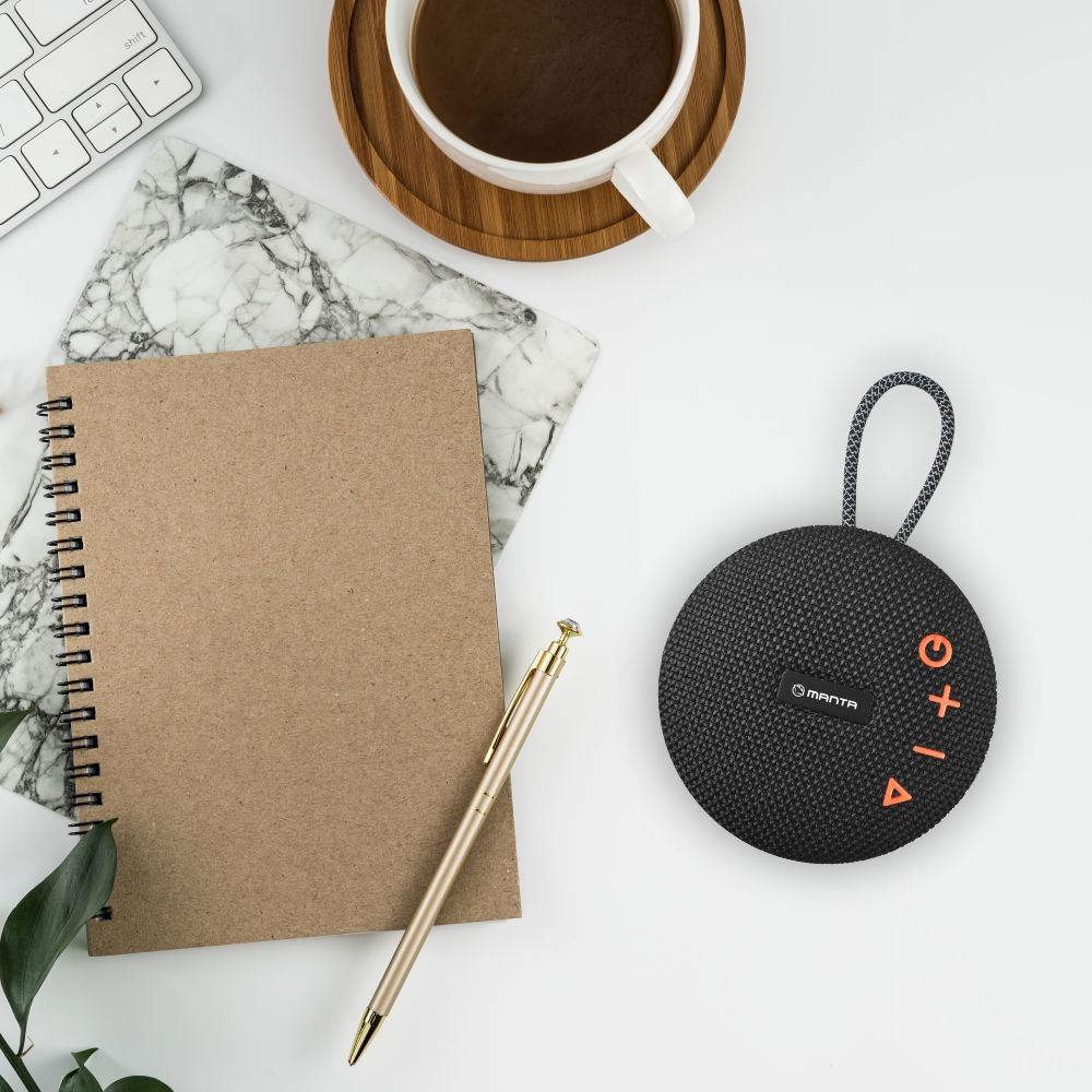 Płaskie zdjęcie przedstawia filiżankę kawy, notatnik, długopis i głośnik na białej powierzchni. Głośnik jest czarny i okrągły.