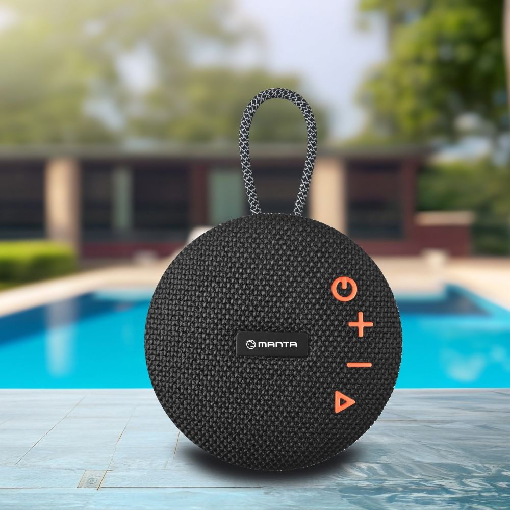 Czarny, okrągły głośnik z pomarańczowymi przyciskami, uchwytem i logo 'MANTA', na tle basenu i domu.
