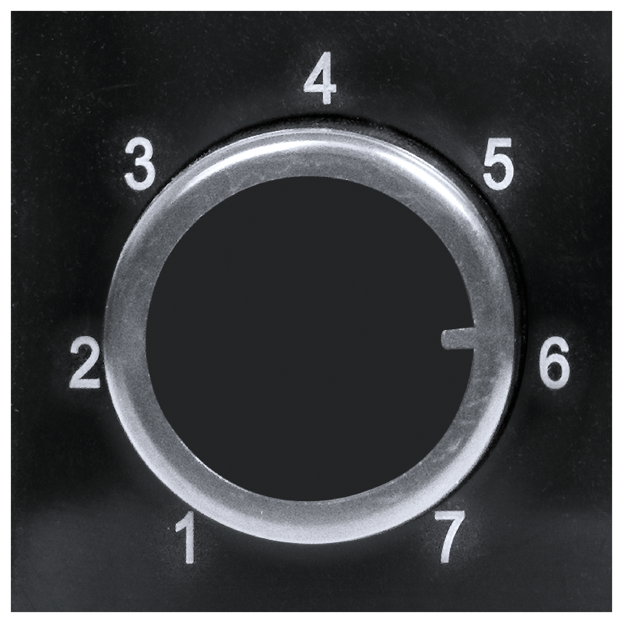 Zbliżenie czarnej tarczy z białymi cyframi 1-7. Srebrny pierścień otacza ciemny środek. Wskaźnik wskazuje na 6.