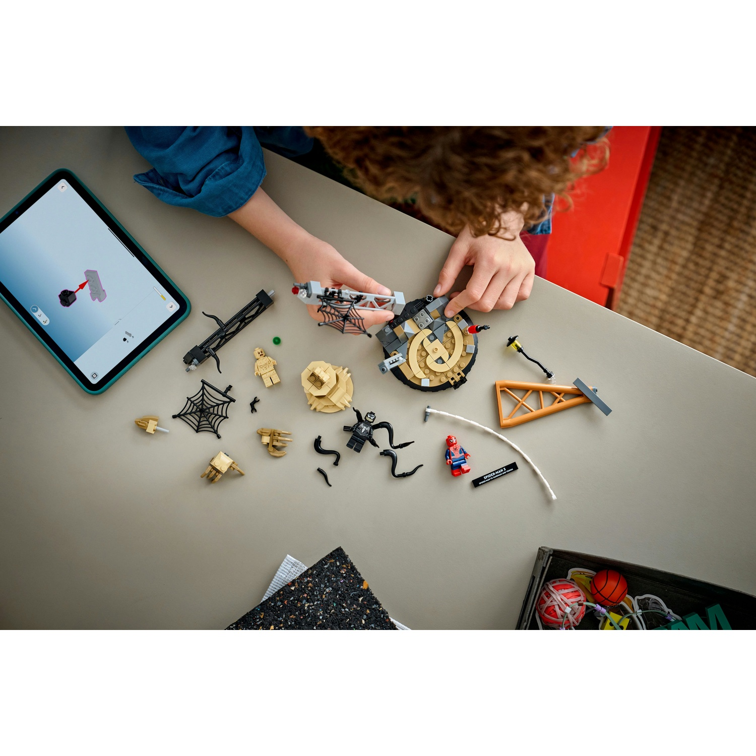 Una persona assembla un set Lego su un tavolo. Pezzi Lego, un tablet con istruzioni e una scatola di giocattoli sono visibili.