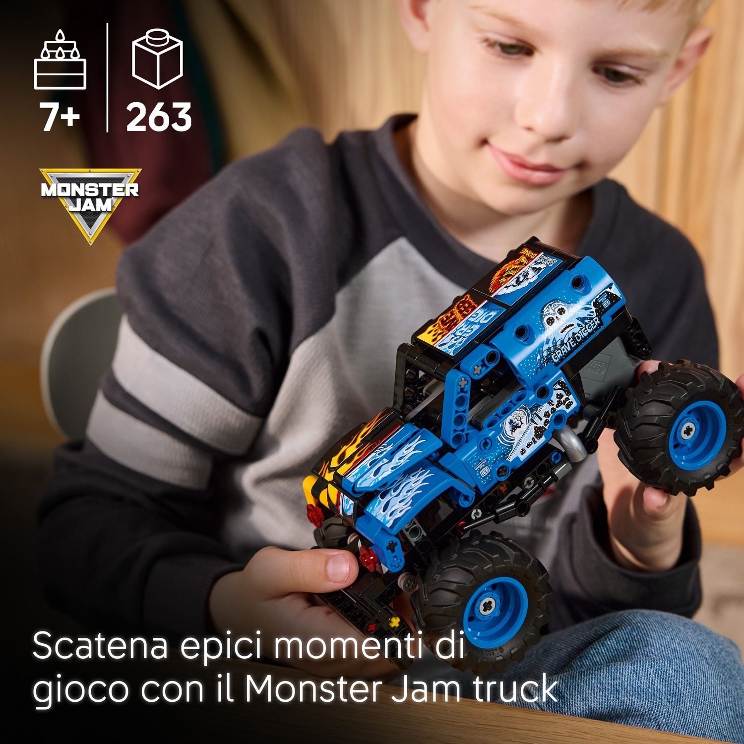 Un ragazzo tiene in mano un monster truck giocattolo blu e nero con l'etichetta Grave Digger. Lo sfondo è sfocato.