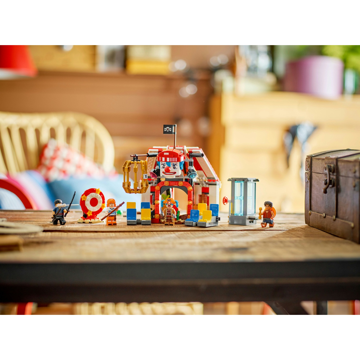 Un set Lego a tema circo con faccia da clown e personaggi su un tavolo di legno. Include un forziere, un bersaglio e altri oggetti di scena.