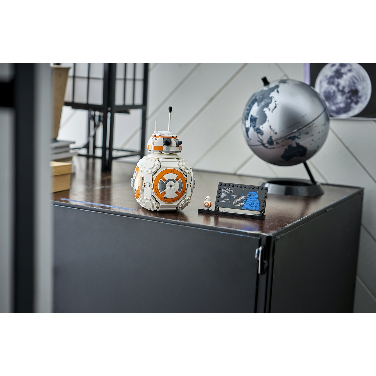 Un set Lego BB-8 su un mobile marrone scuro. Un mappamondo e un'immagine della luna sullo sfondo.