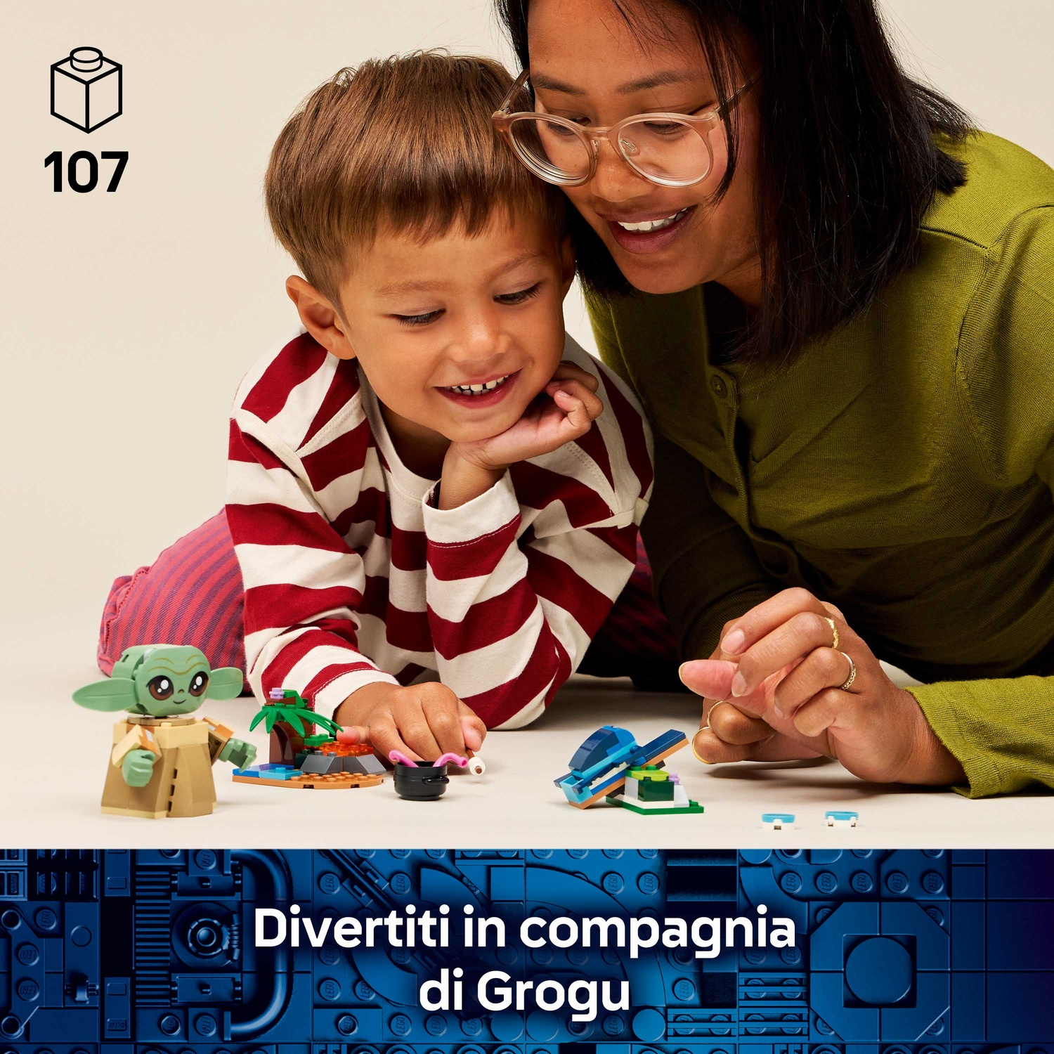 Una donna e un bambino sorridono ai giocattoli LEGO. Una figura di Grogu e altre costruzioni sono sul tavolo. Lo sfondo è blu.