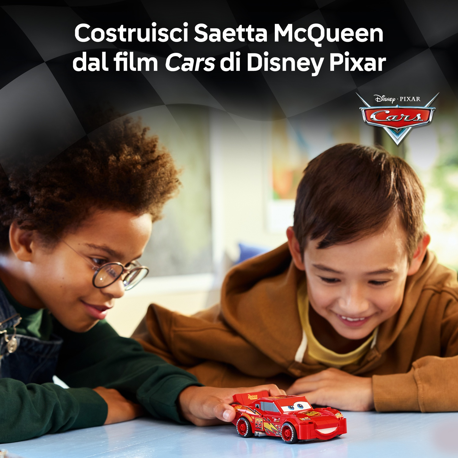 Due ragazzi guardano un'auto giocattolo rossa di Saetta McQueen su un tavolo. L'auto è del film Disney Pixar Cars.