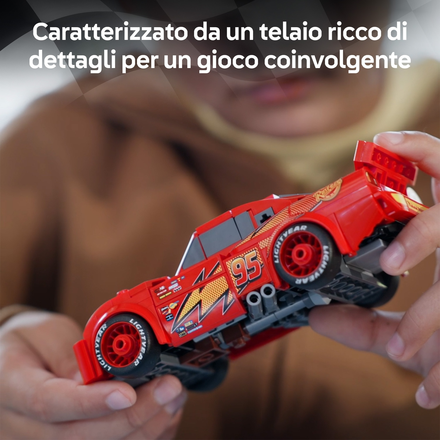 Un'auto giocattolo rossa, tenuta in mano, presenta il numero 95 e grafiche a fulmine. Le ruote dell'auto riportano 'LIGHTYEAR'.