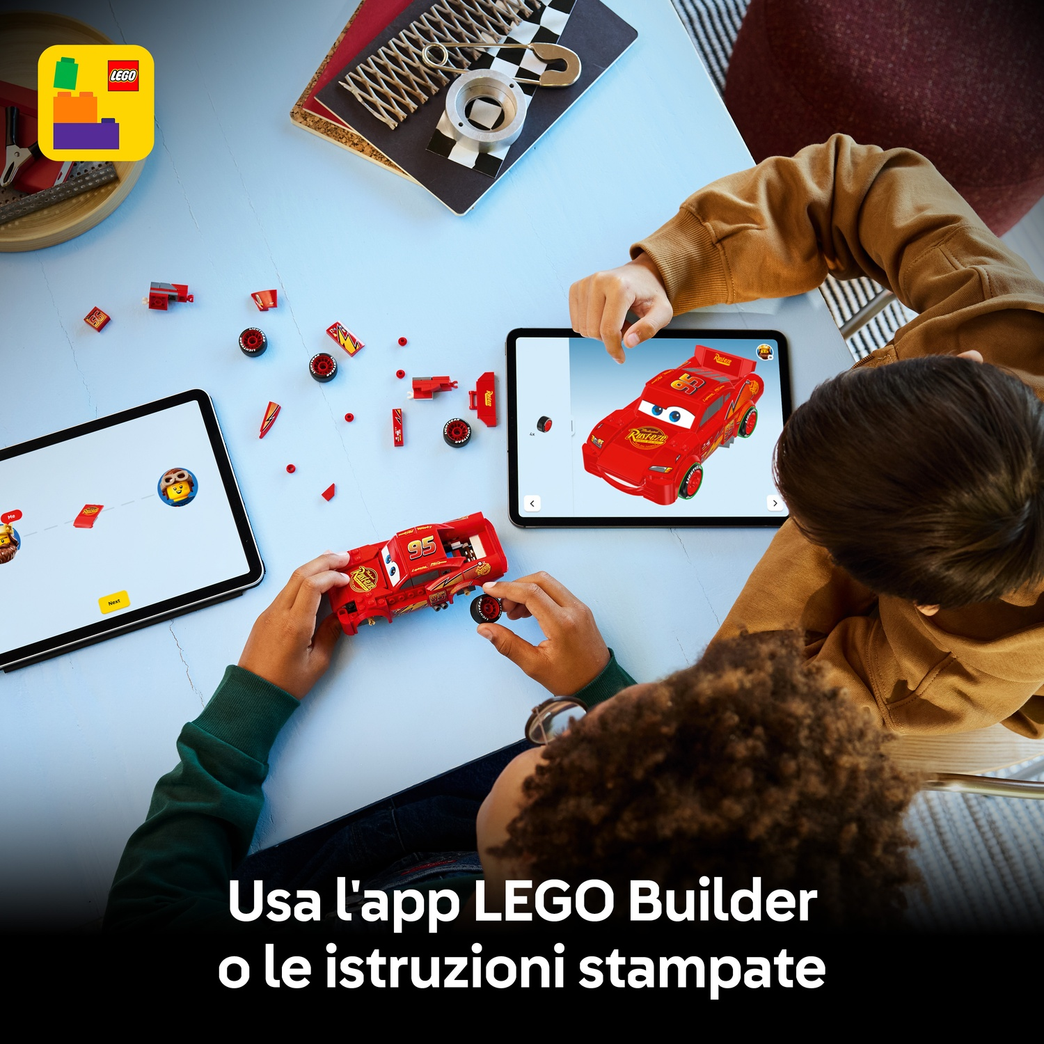 Due bambini assemblano un'auto LEGO rossa Lightning McQueen. I tablet mostrano le istruzioni. Logo LEGO in alto a sinistra.