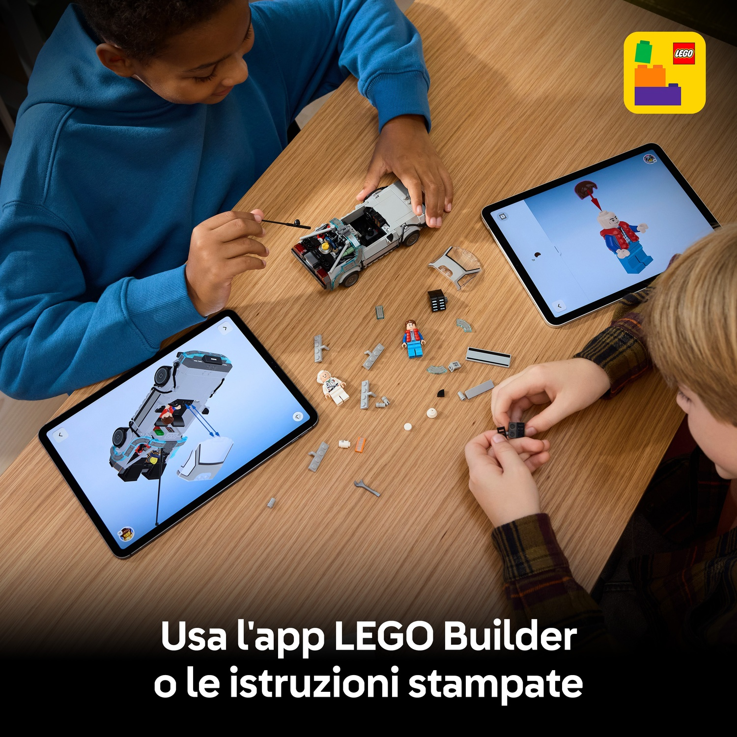Due bambini costruiscono set LEGO, seguendo le istruzioni sui tablet. Auto LEGO parzialmente costruita sul tavolo. Logo LEGO in alto a destra.