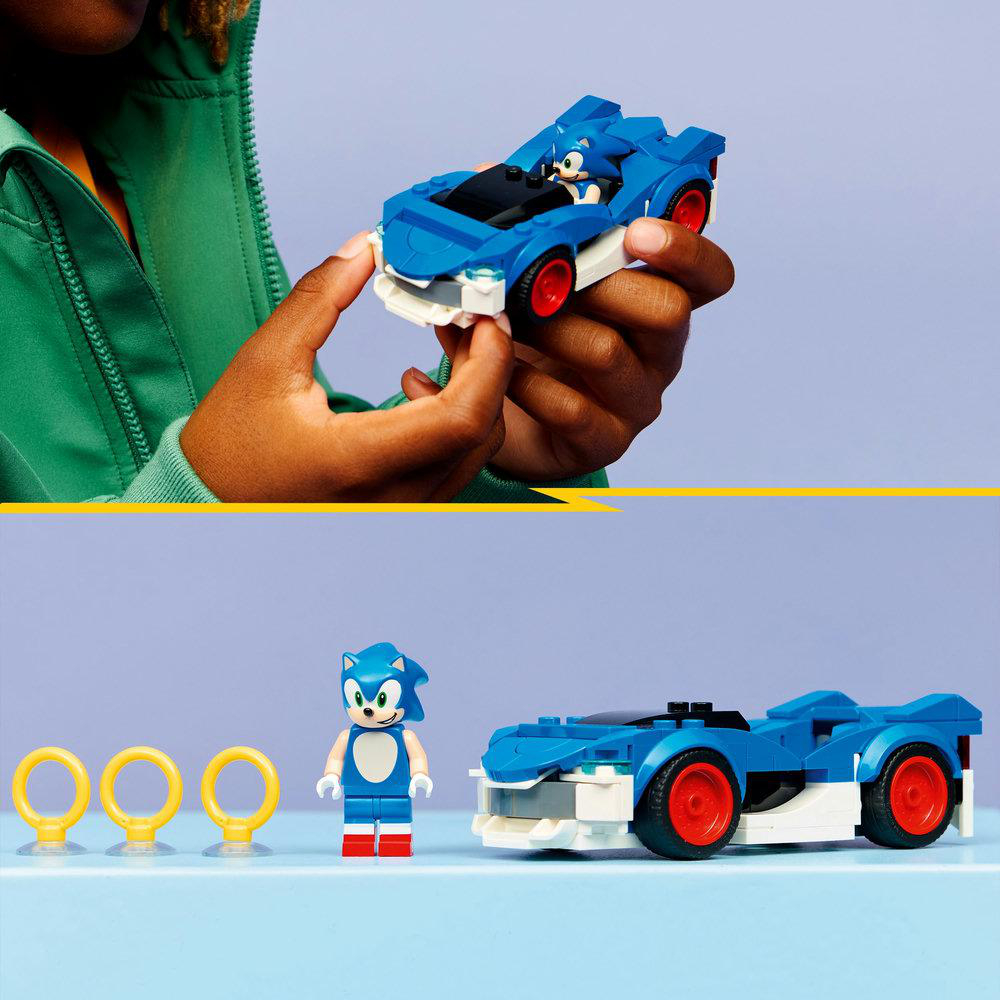 Eine Person hält ein blaues Spielzeugauto mit einer Sonic-Figur darin. Darunter befinden sich eine Sonic-Figur, Ringe und ein Auto auf einer blauen Oberfläche.