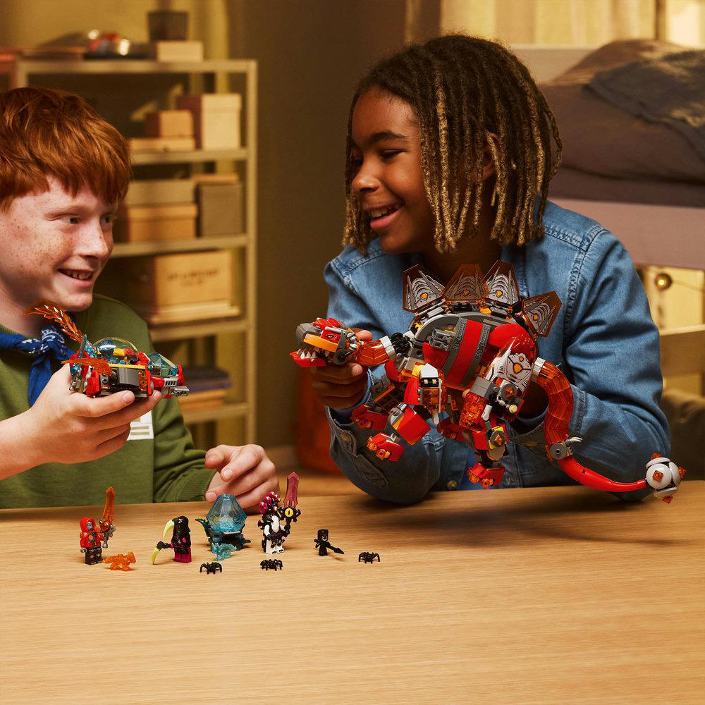 Zwei Kinder lächeln und halten Spielzeugdrachen. Kleine Spielfiguren und Drachen sind auf einem Tisch. Im Hintergrund sind Regale und ein Bett.