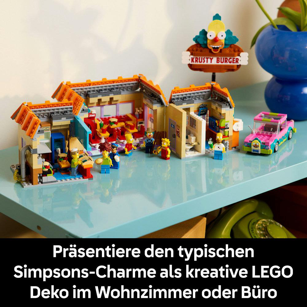 Simpsons-LEGO-Set mit Krusty Burger-Schild, Figuren, einem rosa Auto und bunten Gebäuden auf einer blauen Oberfläche.