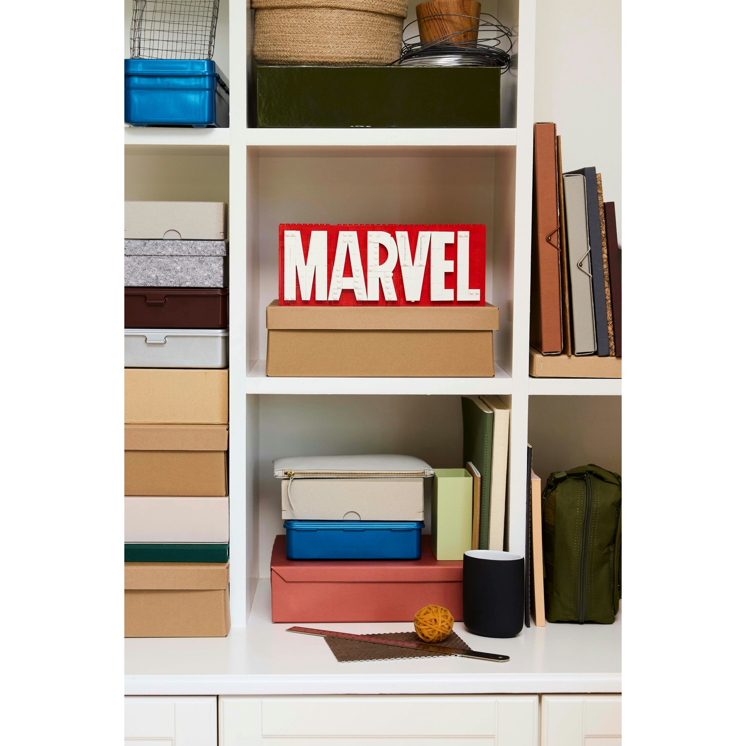 Una mensola bianca con varie scatole, libri e decorazioni. Un cartello rosso 'MARVEL' è su una scatola. Altre scatole sono blu, marroni e verdi.