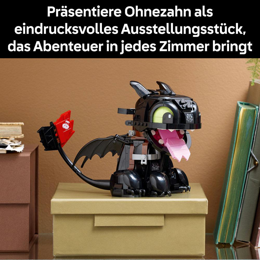 Ein schwarzes Drachenspielzeug mit rosa Zunge und rotem Schwanz steht auf einer braunen Box. Bücher und grüne Pflanze sind im Hintergrund.