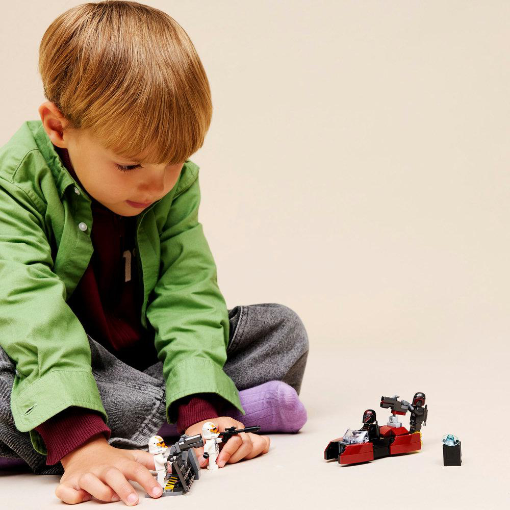 Ein Kind spielt mit Lego Star Wars Sets. Das Kind trägt ein grünes Hemd. Die Sets umfassen einen Speeder und Sturmtruppen.