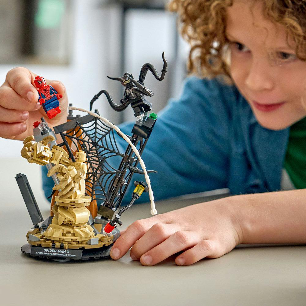 Ein Kind spielt mit einem Spider-Man Lego-Set. Das Set zeigt Spider-Man, Sandman und Venom. Das Kind hält Spider-Man.