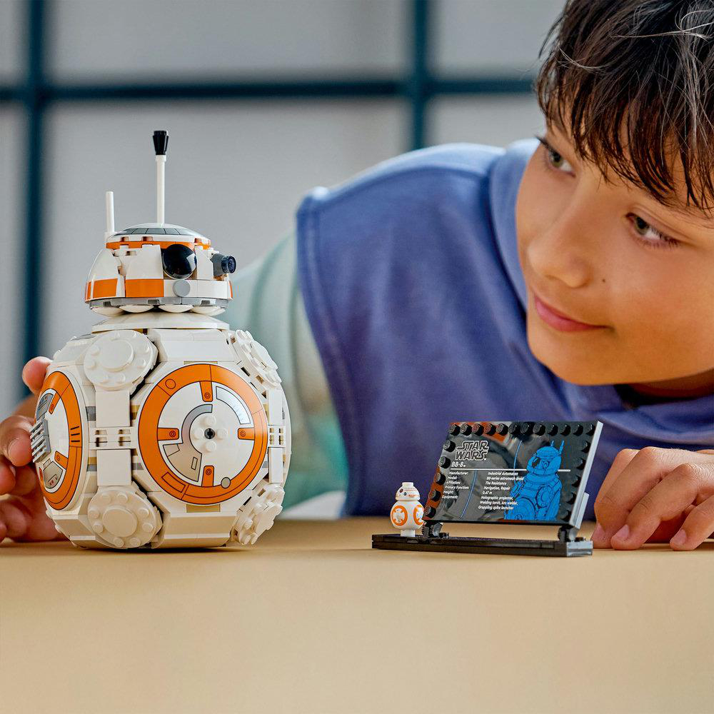 Ein Junge betrachtet ein BB-8 Lego-Set. BB-8 ist weiß und orange. Es gibt einen kleinen BB-8 und eine Star Wars-Infokarte.