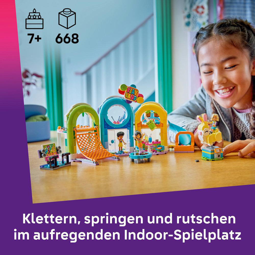 Ein Mädchen lächelt über ein LEGO-Spielset. Das Set zeigt Kletterstrukturen, Figuren und ein 'Play Land'-Schild. Der Hintergrund ist ein Fenster.