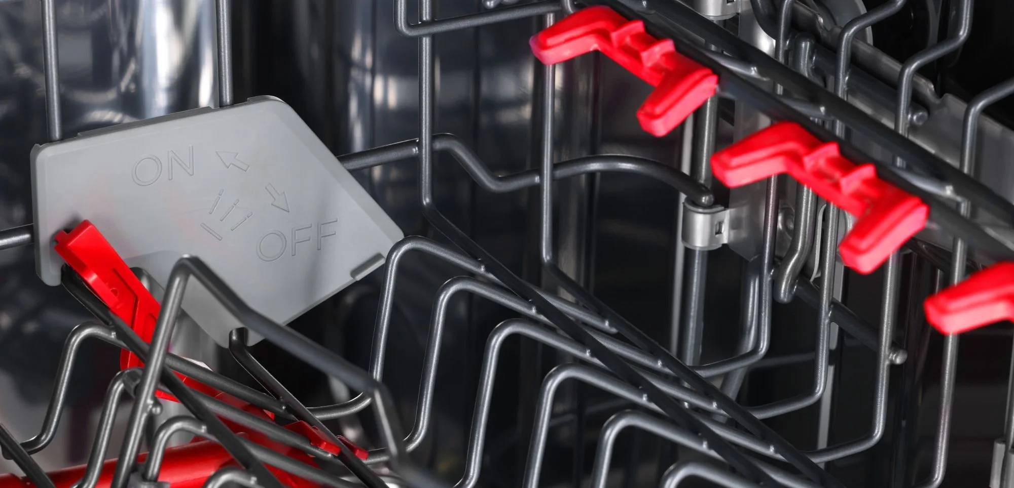 Wnętrze zmywarki, pokazujące ruszt z czerwonymi zatrzaskami i szary panel sterowania z napisami 'ON' i 'OFF'.