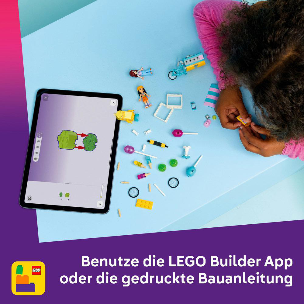 Ein Kind baut mit LEGOs. Ein Tablet zeigt Anweisungen. Verschiedene LEGO-Teile und Mini-Figuren sind auf einer blauen Oberfläche verstreut.