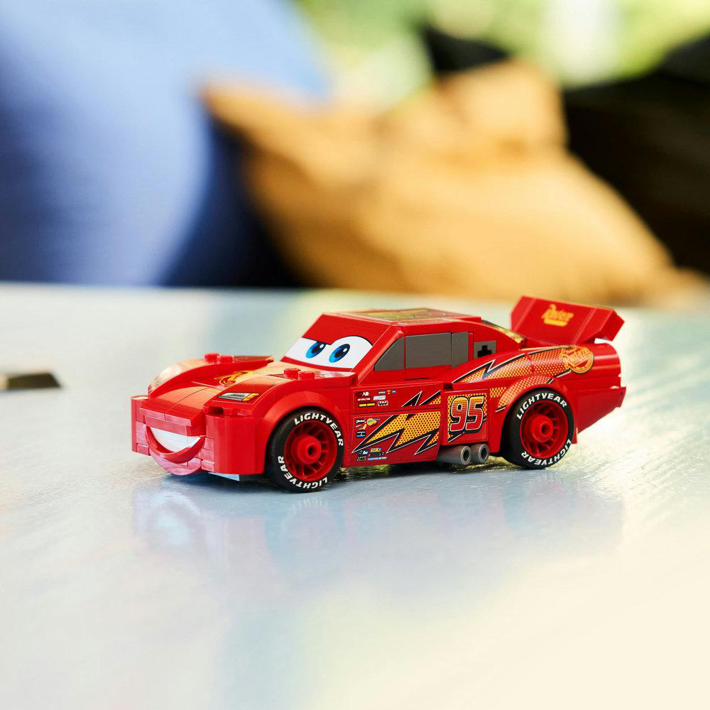 Ein rotes Spielzeugauto, Lightning McQueen, steht auf einer weißen Oberfläche. Es hat blaue Augen, die Nummer 95 und 'LIGHTYEAR' auf den Rädern.