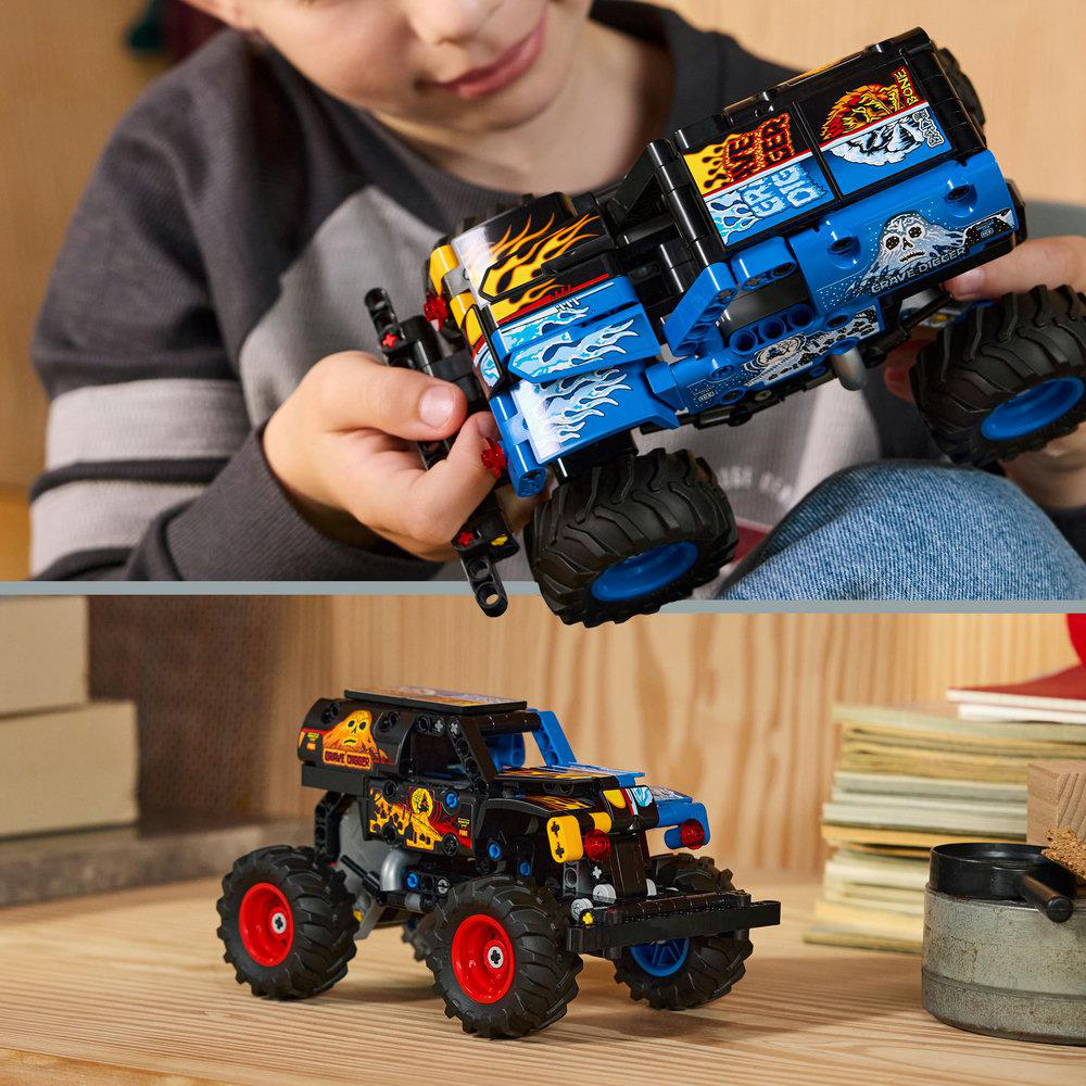 Ein Kind hält einen blau-schwarzen Spielzeug-Monstertruck mit großen Reifen. Ein weiterer Monstertruck steht auf einer Holzoberfläche.