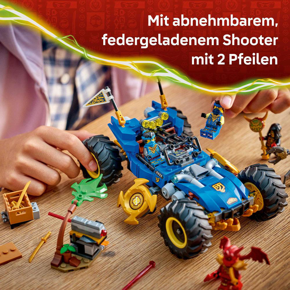 Blaues Lego-Auto mit gelben Akzenten. Eine Hand hält eine Lego-Figur. Weitere Lego-Figuren und Zubehörteile liegen auf Holz.