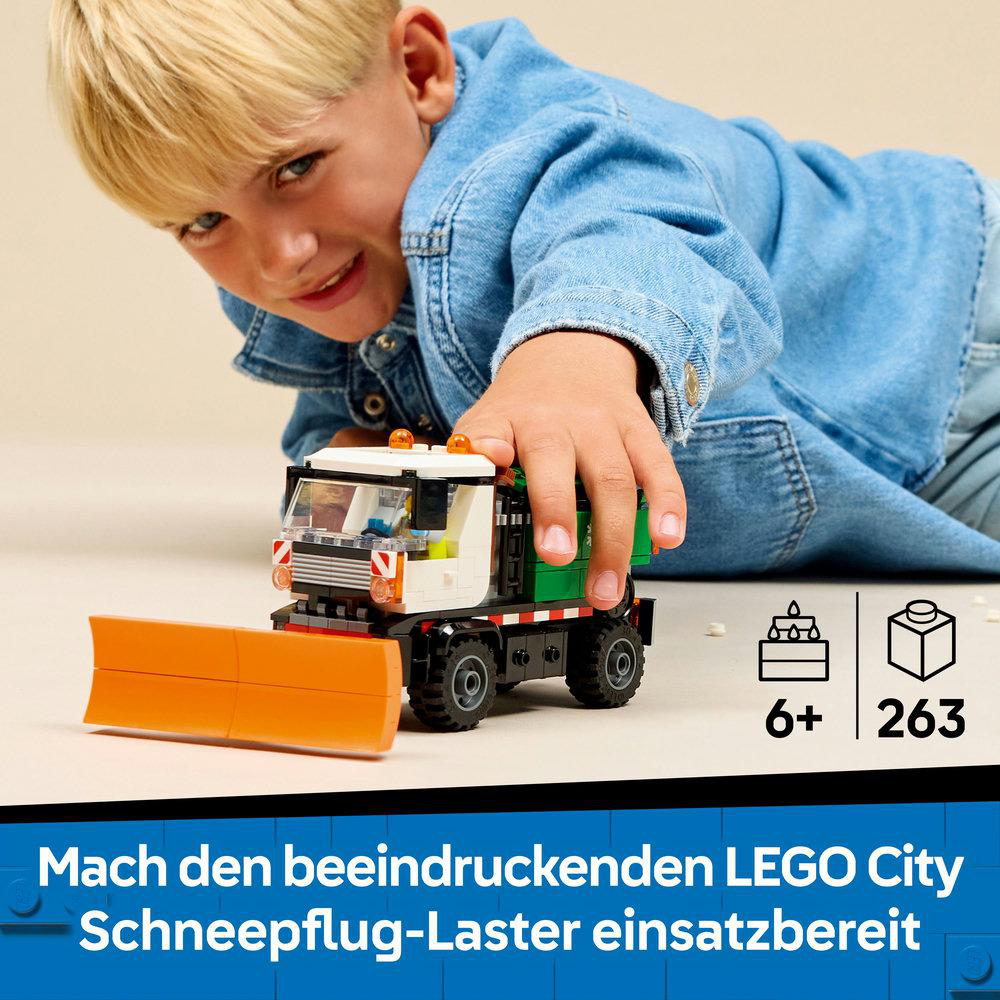 Ein Junge spielt mit einem Lego-Schneepflug. Der LKW ist weiß, grün und schwarz mit einem orangefarbenen Pflug. Der Hintergrund ist blau.