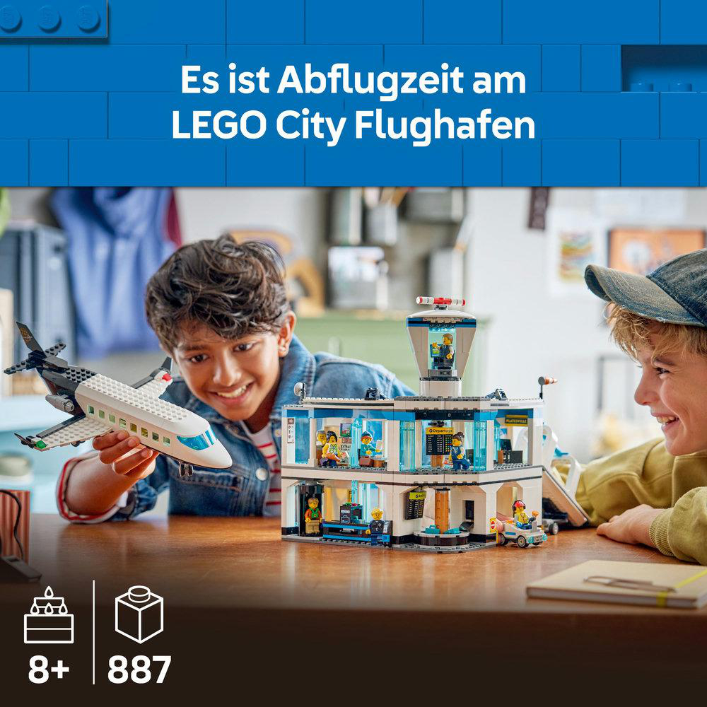 Zwei Jungen spielen mit einem LEGO-Flughafenset. Einer hält ein Flugzeug, der andere lächelt. Das Set zeigt einen Kontrollturm, ein Terminal und Fahrzeuge.